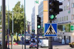Liikennevalot vihreällä suojatien vieressä, taustalla kaupungin katu ja autoja.