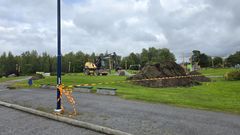 Grävmaskin och avspärrat område i park.