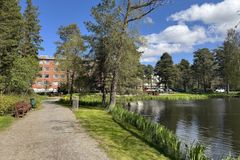 Gångväg vid en sjö med träd och ett flerbostadshus i bakgrunden under en solig dag.