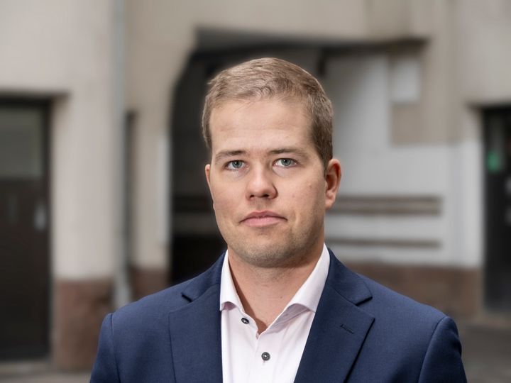En man i kostym står framför en suddig bakgrund.