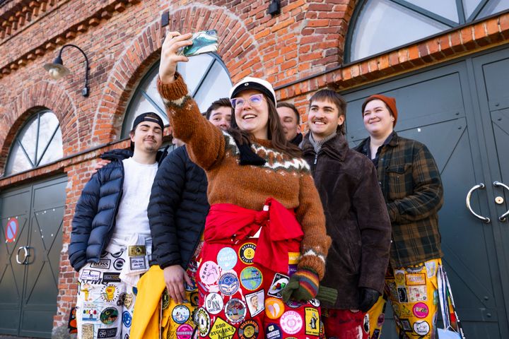Fyra studerande går utomhus under en solig dag iförda studenthalare fyllda med märken och färger. Träden i bakgrunden är kala.