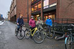 Fyra personer med cyklar står på en asfalterad väg framför en tegelbyggnad. De har cykelhjäl
