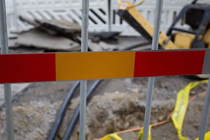 Rakennustyömaa, jossa kaivettu maata, metalliaidalla suljettu alue ja kone taustalla.