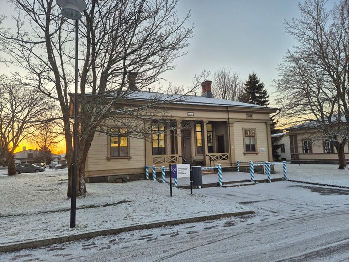 Gult trähus i vinterskrud med snö på marken och solnedgång i bakgrunden.