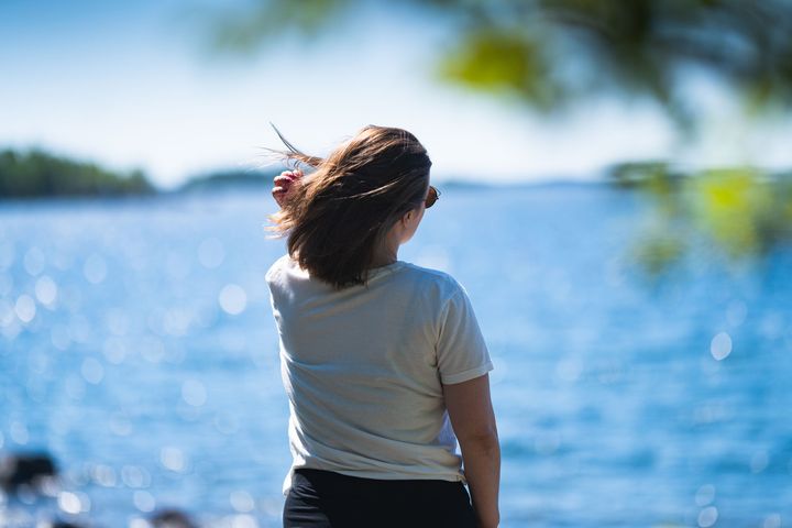 Kvinna med solglasögon står vid en sjö och ser ut över vattnet.