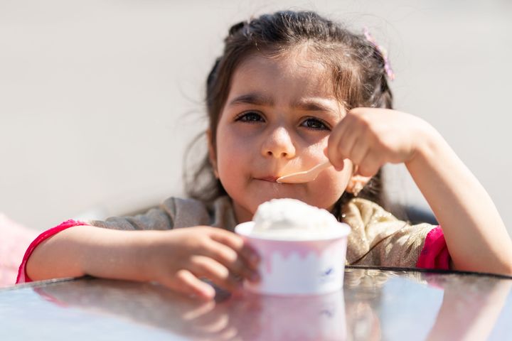 Flicka äter glass med sked utomhus.