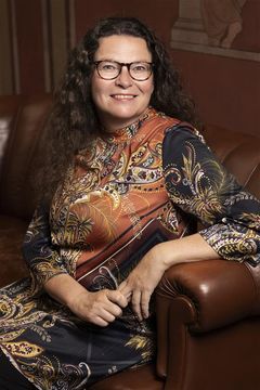 Nainen istuu nahkaisella sohvalla, yllään koristeellinen paita.