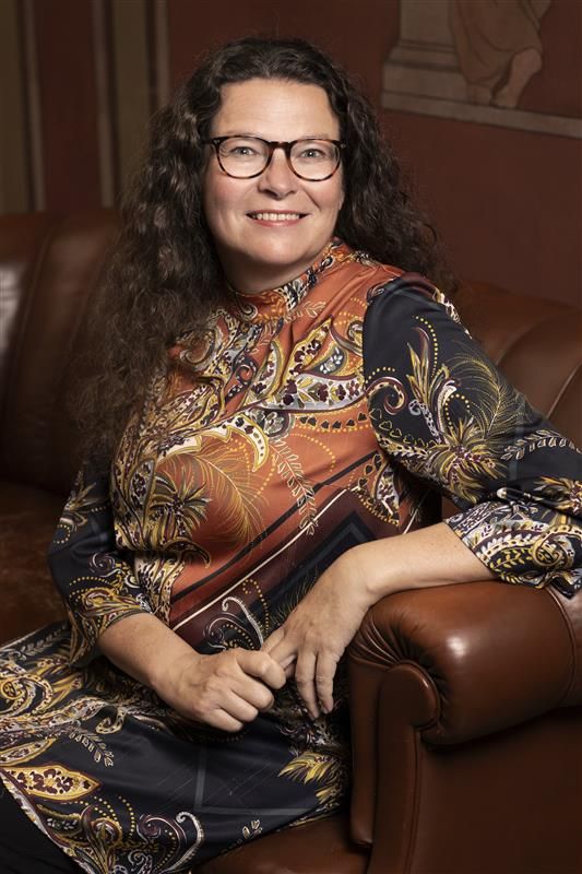 Nainen istuu nahkaisella sohvalla, yllään koristeellinen paita.