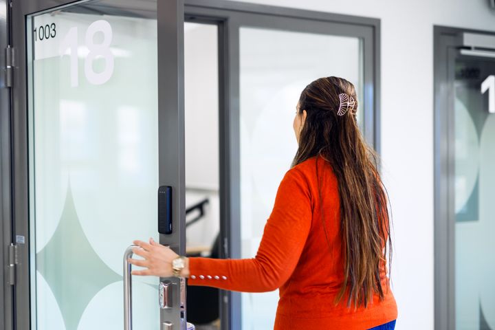 Nainen avaa lasiovea toimistoon.