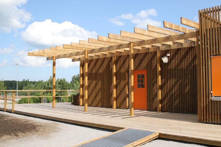 En byggnad med träpanel och pergola under en klarblå himmel.