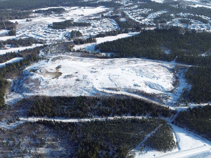 Ilmakuva talvisesta ylijäämämaan vastaanottopaikasta, jossa näkyy metsäalueita ja lumen peittämiä teitä.