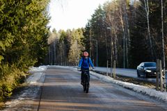 Henkilö pyöräilee talvitakissa metsäisellä pyörätiellä, vieressä kulkee autotie.