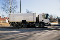 Gatustädningsfordon som parkerat vid trottoar på en solig dag.