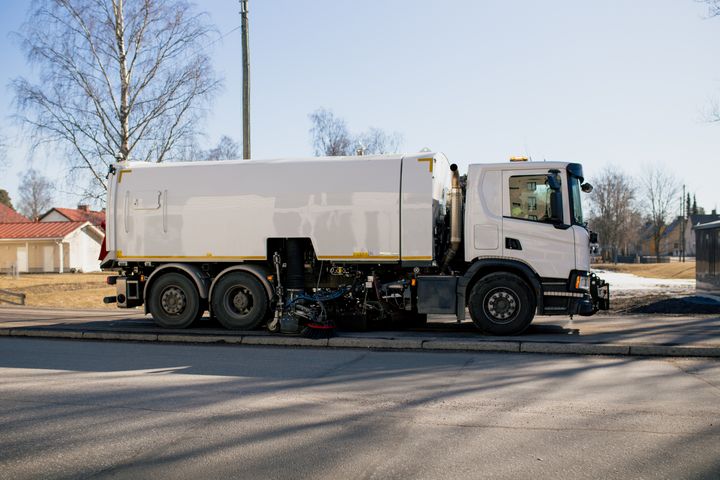 Gatustädningsfordon som parkerat vid trottoar på en solig dag.