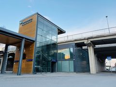 Moderni linja-autoaseman rakennus, jossa on lasiseinät ja puiset yksityiskohdat. Taustalla on kävelysilta.