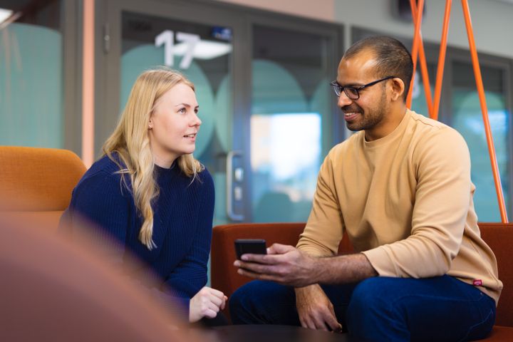 En kvinna och en man samtalar vänligt på en soffa, mannen håller en mobiltelefon.