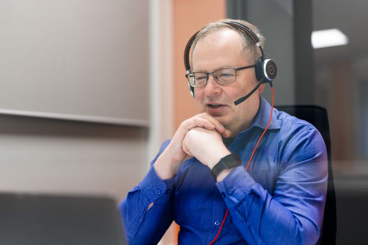 Mies käyttää kuulokkeita videopuhelussa.