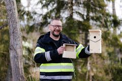 Arbetsledare i reflexjacka visar upp två fågelholkar i trä bland träd.