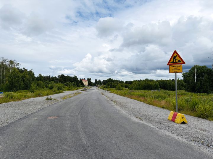 Väg med skylt som varnar för byggarbetsplatstrafik, omgiven av grönska.