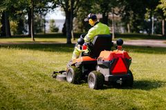 Henkilö ajaa päältä ajettavalla ruohonleikkurilla nurmikolla puistossa.