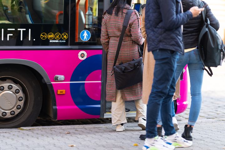 Ihmisiä nousemassa vaaleanpunaiseen bussiin.