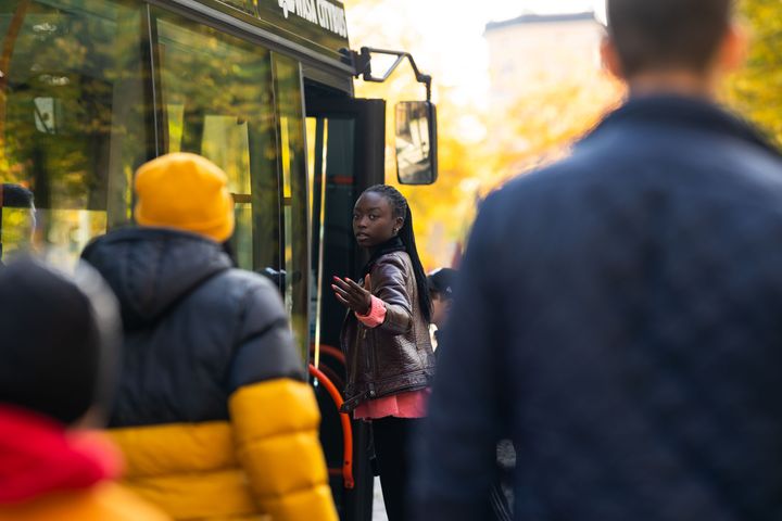 Henkilö astumassa bussiin syksyisessä säässä. Muita henkilöitä odottaa vuoroansa hänen takanaan.