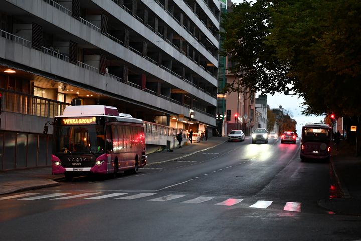 Stadsgata i skymningen med Liftis buss; människor väntar på trottoaren.