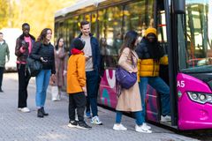 Ihmisiä nousemassa vaaleanpunaiseen bussiin kaupungin kadulla.