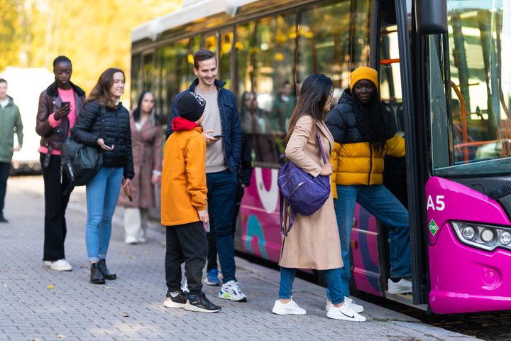 Personer som väntar och går ombord på en buss vid en hållplats.