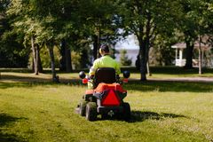 En person kör en gräsklippare över en gräsmatta i en park med träd i bakgrunden.