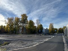 Syksyinen katunäkymä: puiden reunustama tie, uusi asfaltti ja rakennuksia taustalla.