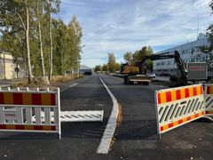 Vägarbete på en industrigata med avspärrningar och en grävmaskin.