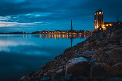 Ilta-auringon valaisema Vaasan rantamaisema, tyyni meri ja kaupungin valot heijastuvat veteen.