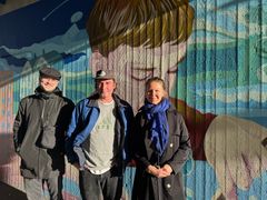 Tre personer framför den färgstarka Green Leaf-muralen med ett stort målat ansikte.