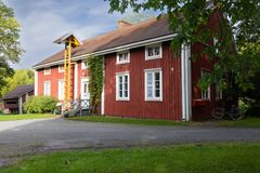 Punainen puutalo valkoisin ikkunankehyksin, keltaiset tikkaat julkisivulla ja sorapiha edessä.