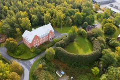 Flygbild av en stor tegelbyggnad omgiven av höstskog, med en rund gräsyta inramad av häck och mindre hus i närheten.