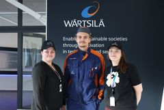 Kuvassa Wärtsilä-seinän edessä seisovat kolme ihmistä: Team lead Serafia Mannila, oppisopimusopiskelija Samu Jokinen ja Tertta Kentta, Competence Specialist.