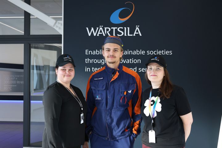 Kuvassa Wärtsilä-seinän edessä seisovat kolme ihmistä: Team lead Serafia Mannila, oppisopimusopiskelija Samu Jokinen ja Tertta Kentta, Competence Specialist.