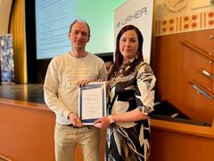 Two people standing in a conference room holding a document together.