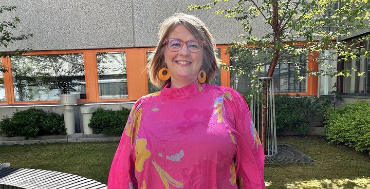 "Anna-Mari Simunaniemi, standing in the courtyard of Vaasa University of Applied Sciences in a red blouse, smiling."
