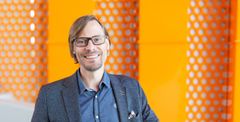 "VAMK's President and CEO Hannu Vahtera smiling in front of an orange background on campus."