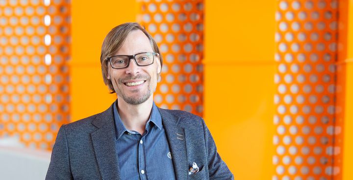 "VAMK's President and CEO Hannu Vahtera smiling in front of an orange background on campus."