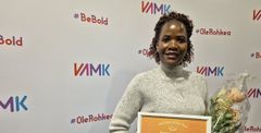 Person holding an award and flowers, standing in front of a VAMK backdrop.