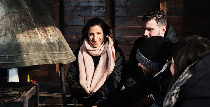 A group of people sitting together, wearing winter clothing, inside a wooden structure.