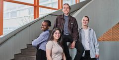 A group of four students smiling on indoor stairs.
