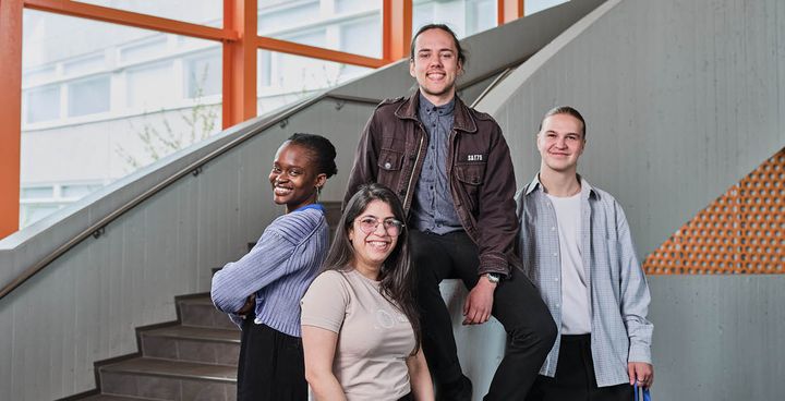 A group of four students smiling on indoor stairs.