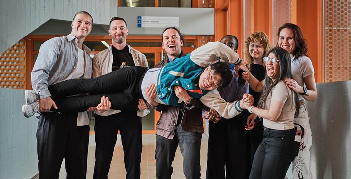 A group of smiling people, with one person playfully held up by others.