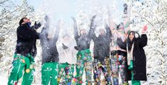 A group of people in colorful outfits joyfully throwing snow in the air.