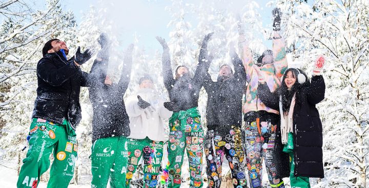 A group of people in colorful outfits joyfully throwing snow in the air.