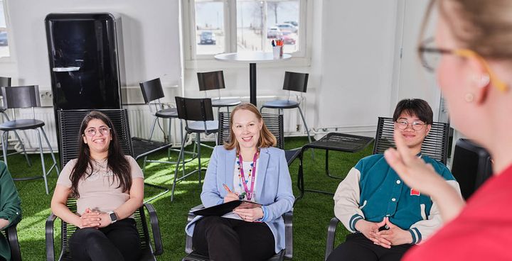 Kolme henkilöä istuu yhdessä ja kuuntelee toista henkilöä sisätiloissa.